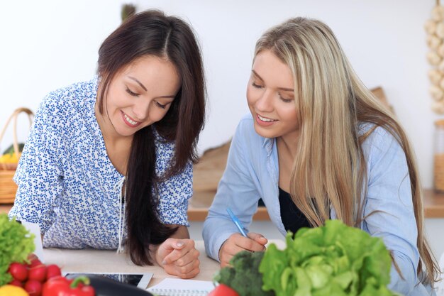 Two young happy women are making online shopping by tablet computer and credit card Friends are going to cook in the kitchen