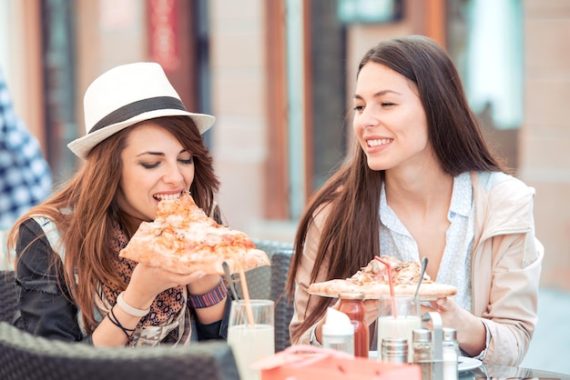 Two young happy women eating pizza outdoors