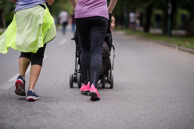 две молодые здоровые женщины бегают вместе, толкая детскую коляску в городском парке
