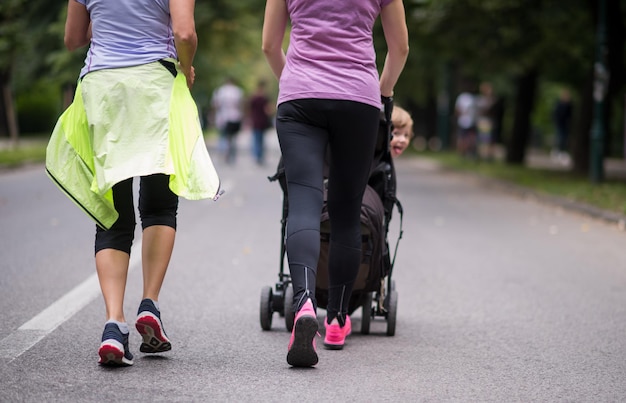 two young healthy women jogging together while pushing a baby stroller at city park