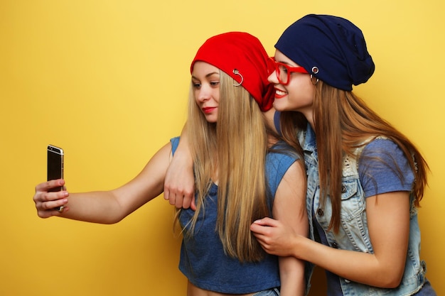 Two young hipster girls friends taking selfie over yellow background