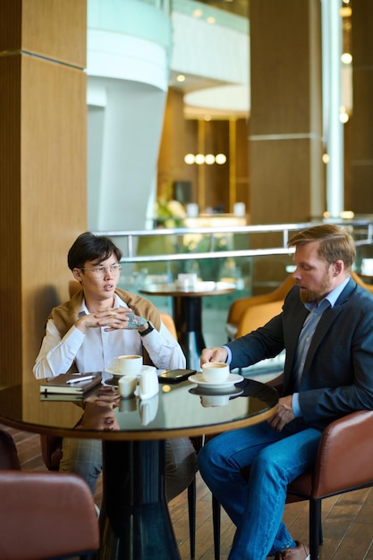 Two young interracial businessmen in formalwear having coffee in cafe