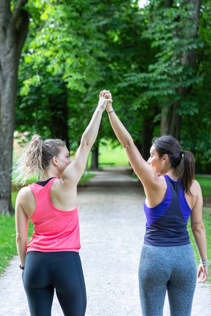 두 젊은 여인 이 공원 에서 팔 을 들고 크로스 피트 운동 을 한 후 축하 하고 있다