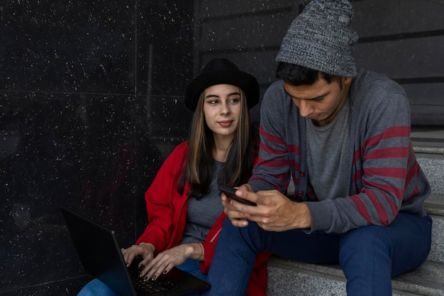 Two young Latin American brothers sitting on the stairs with laptop and cell phone