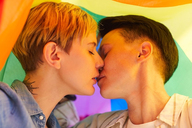 Photo two young lesbians kissing each other under the colored flag