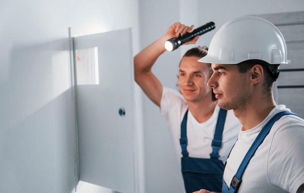 Foto due giovani elettricisti maschi lavorano insieme all'interno usando la torcia elettrica