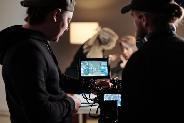 Two young men in black shirts adjusting focus of camera during shooting