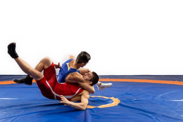 Two young men in blue and red wrestling tights are wrestlng and making a suplex wrestling on a yellow wrestling carpet in the gym