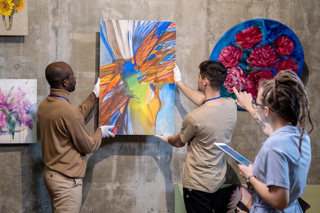 Two young men hanging abstract painting on wall