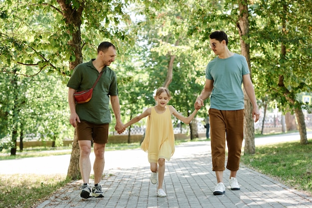 공원에서 산책하는 동안 어린 소녀와 손을 잡고 있는 두 젊은 남자