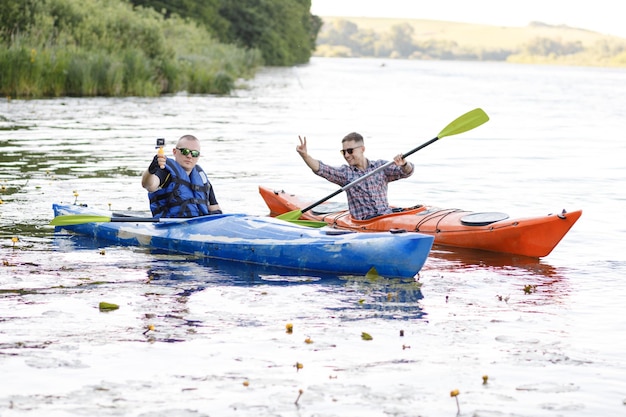 Two young men sit in kayaks and take a selfie with a portable camera The concept of water entertainment