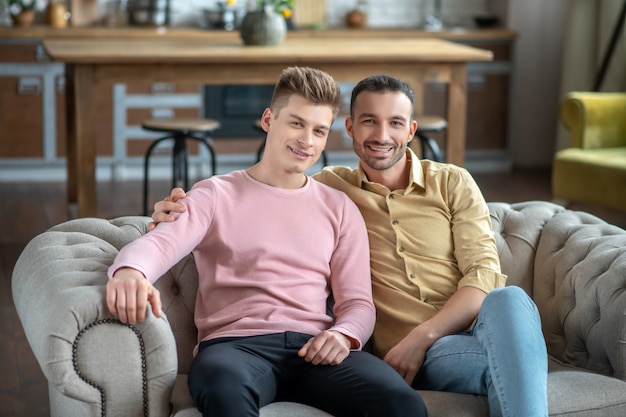 Photo two young men sitting on the sofa looking happy