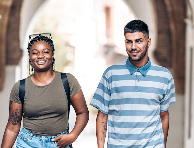 Two young people of different ethnicities smiling as they stroll through the streets of a city.