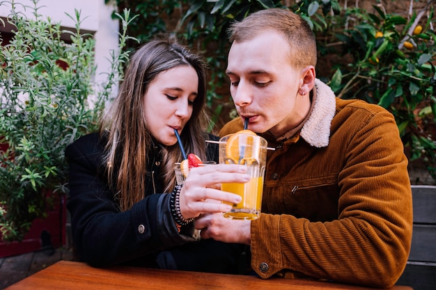 Two young people drinking a natural fruit smoothie from a straw in a bar