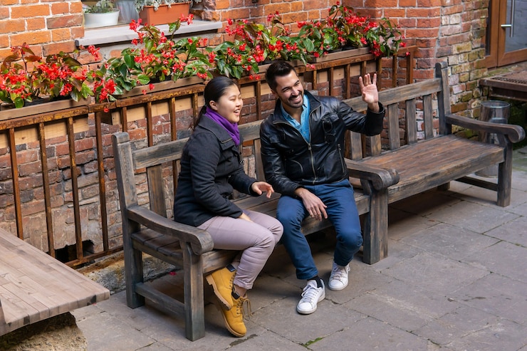 Photo two young people a guy and a girl sitting on a bench outdoors greet someone