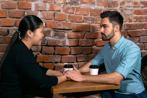 Two young people a guy and a girl talking holding hands in a coffee shop on the background of a rough brick wall