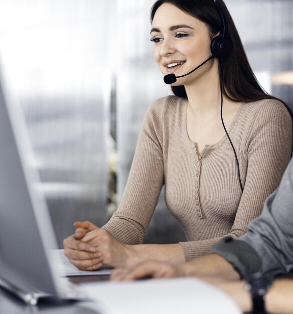 Two young people in headsets are talking to the clients while sitting at the desk in an office Focus on woman Call center operators at work