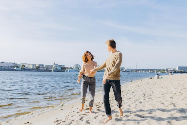 Two young people in love running on the beach They smile at each other Beautiful couple holding hands Beach Feeling Dress in a sweater