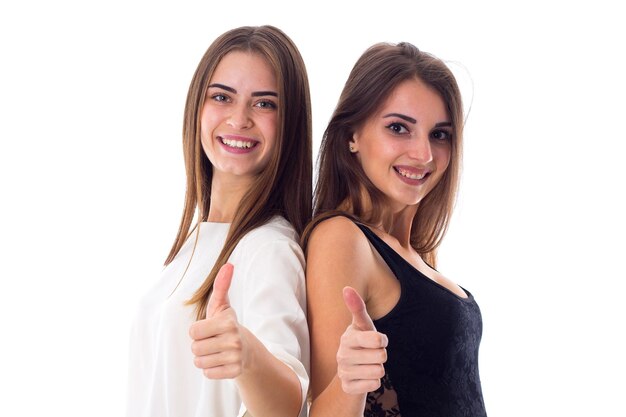 Two young positive women in black and white shirts showing thumbs up on white background in studio