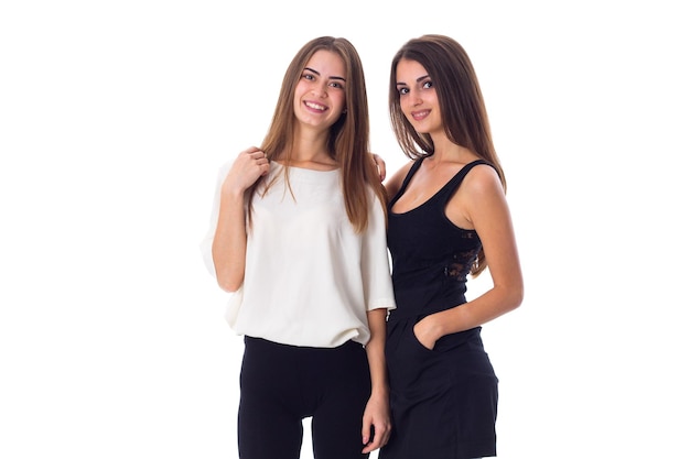 Two young positive women in black and white shirts smiling on white background in studio