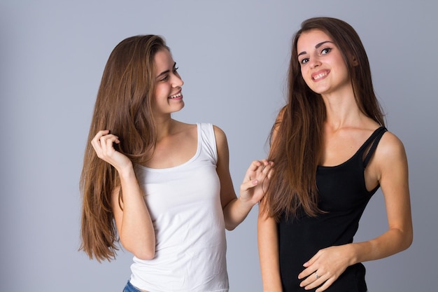 Two young positive women in black and white shirts standing on gray background in studio