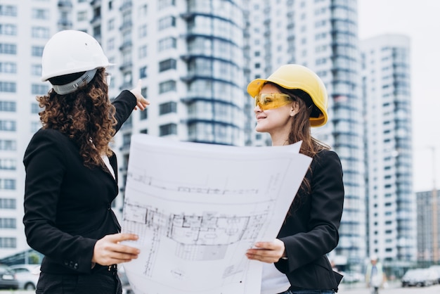 Foto due giovani graziosi imprenditori industriali ingegneri industriali in caschi da costruzione su uno sfondo di costruzione di vetro. piano di costruzione, architetto, progettista, riuscito