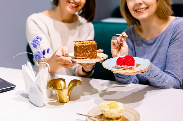 Two young pretty female friends having fun and eating desserts at bakery or pastry shop