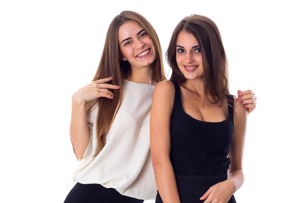 Two young pretty women in black and white shirts embracing on white background in studio