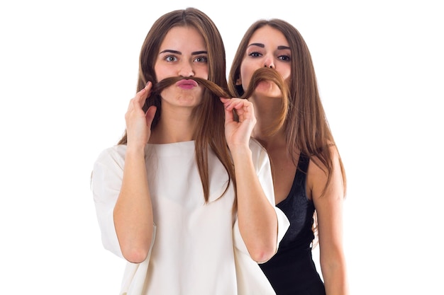 Photo two young pretty women in black and white shirts making moustache of their hair in studio