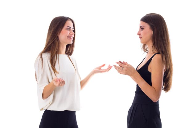 Two young pretty women in black and white shirts talking on white background in studio