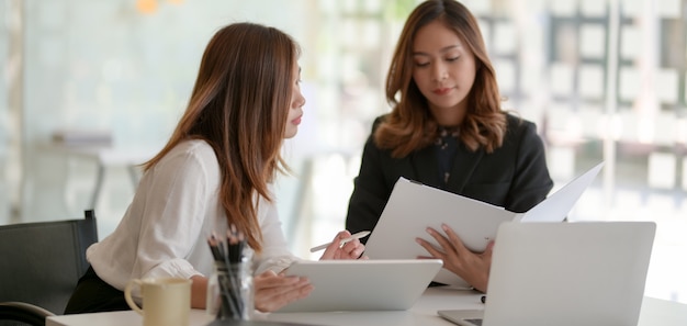 Two young professional businesswomen consulting the project plan together in modern office