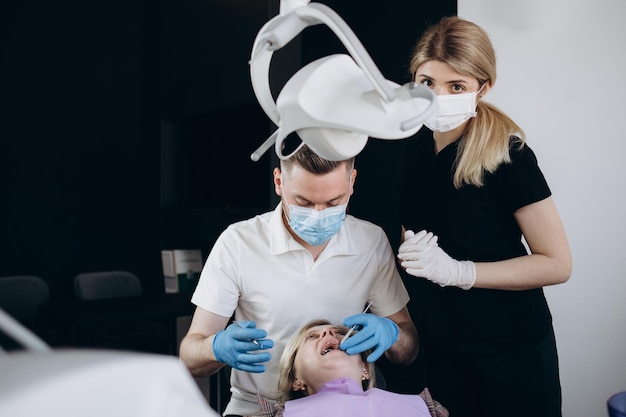 Два молодых профессиональных стоматолога в перчатках и белых халатах смотрят на вас со своего рабочего места с медицинским оборудованием