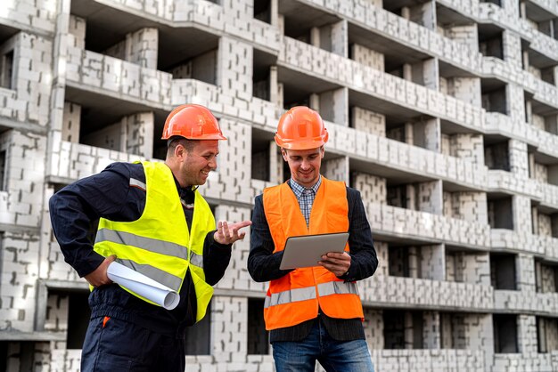 Due giovani lavoratori intelligenti in uniforme in piedi in un cantiere che discutono di un progetto di casa. concetto di costruzione