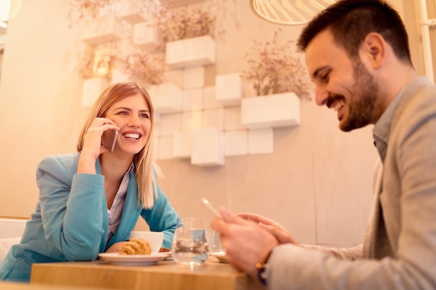 Два молодых улыбающихся бизнесмена на перерыве в кафе. Человек, работающий за планшетом. Женщина с помощью смарт-телефона. Они пьют кофе и завтракают. Выборочный фокус.