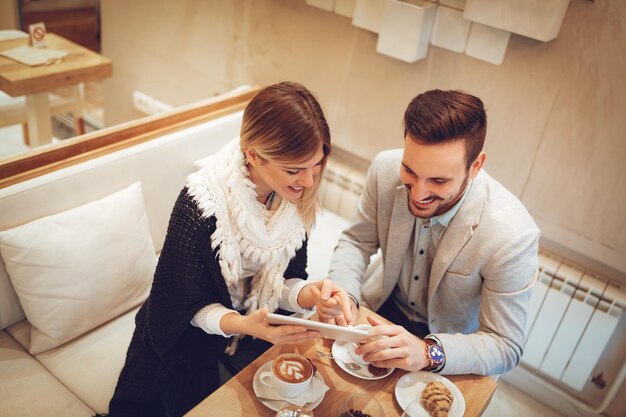 Two young smiling businesspeople talking and working on digital tablet on a coffee break at cafe. Top view.