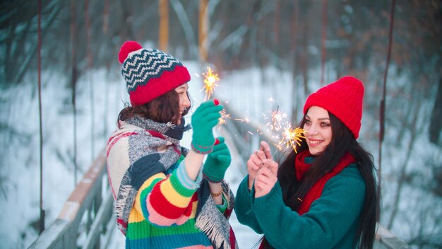 Two young smiling women standing on the bridge holding sparklers and having fun