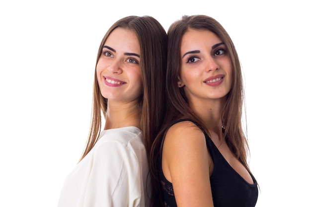 Two young smiling women in white and black shirts standing back to back on white background