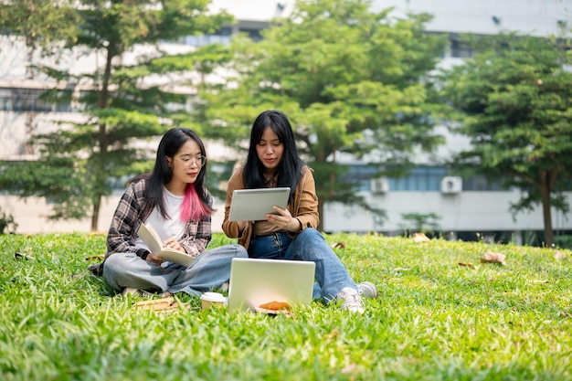 Foto due giovani studenti sono seduti sull'erba in un parco a discutere di qualcosa su un tablet digitale