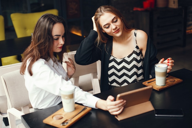Two young stylish businesswomen sitting in a cafe and use the tablet