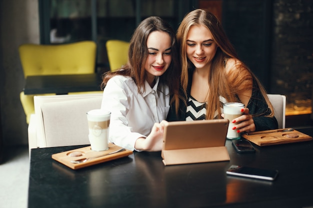 Two young stylish businesswomen sitting in a cafe and use the tablet