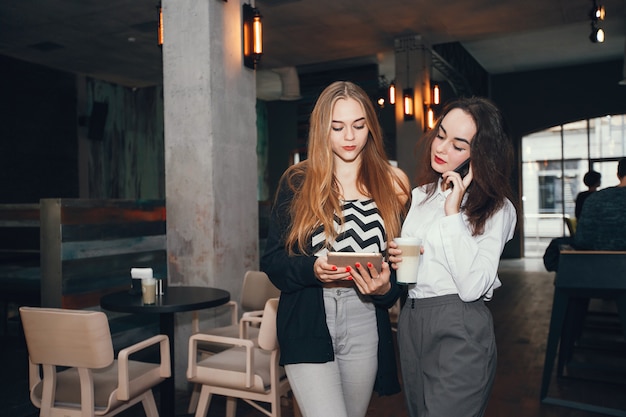 Фото Две молодые стильные предприниматели, стоя в кафе и использовать планшет