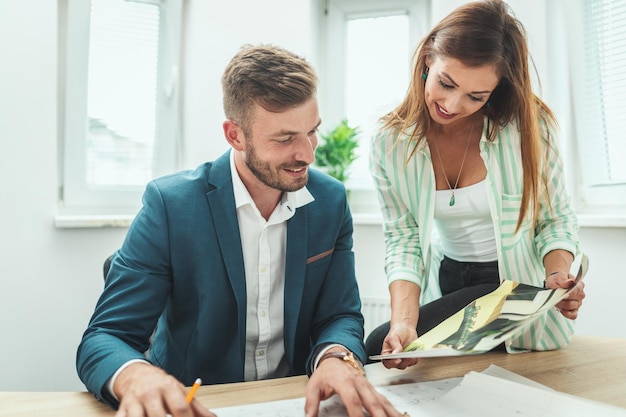 Two young successful architects are working on a new project and communicating while analyzing blueprints in the office.