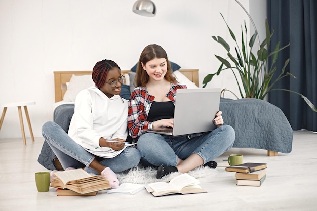 Two young teenage girls sitting on a floor near bed studying and using a laptop