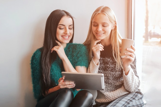 Due giovani donna in chat in una caffetteria. due amici che si godono il caffè insieme. una ragazza usa un tablet