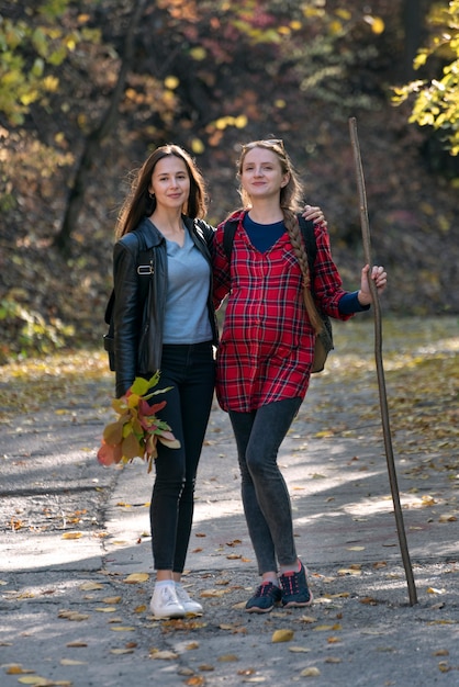 Две молодые женщины стоят в осеннем парке и наслаждаются солнечным днем. Дружба и общение. Вертикальная рамка