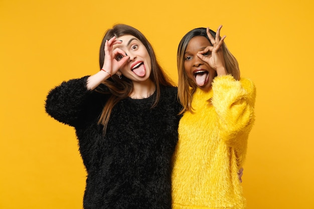 Two young women friends european and african american in black yellow clothes standing posing isolated on bright orange wall background, studio portrait. people lifestyle concept. mock up copy space