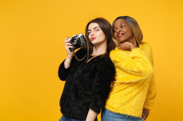 Две молодые женщины-друзья европейка и афроамериканка в черно-желтой одежде стоят, позируя изолированно на ярко-оранжевом фоне стены, студийный портрет. Концепция образа жизни людей. Скопируйте пространство для копирования.