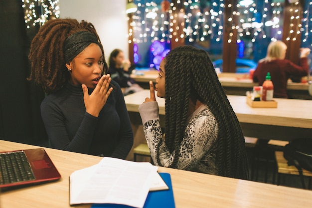 Two young women gossip at table