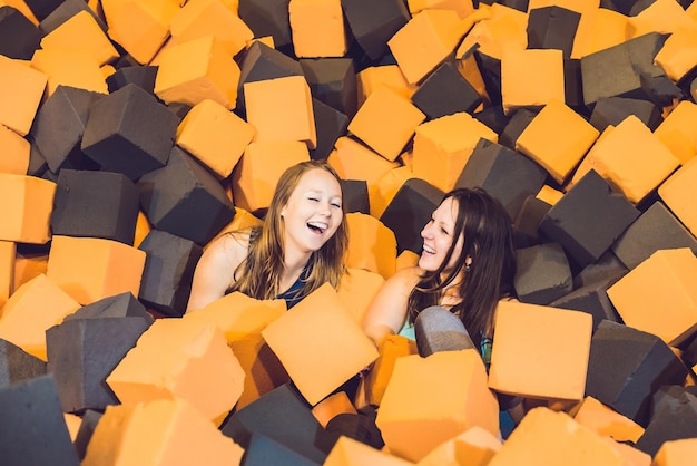 Две молодые женщины веселятся с мягкими кубиками на закрытой детской площадке в яме из поролона в батутном центре