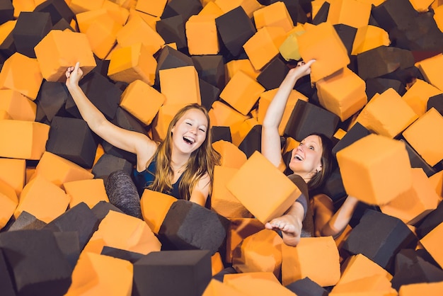 Two young women having fun with soft blocks at indoor children playground in the foam rubber pit in